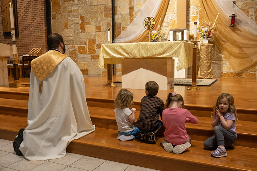 Deacon Robert Lawson prayed with children, including 4-year-old Natalie Claudin (right), gathered near the altar during eucharistic adoration at a Young Families Holy Hour April 25 at Incarnate Word in Chesterfield. Deacon Lawson will be ordained to the priesthood May 25 at the Cathedral Basilica of Saint Louis.